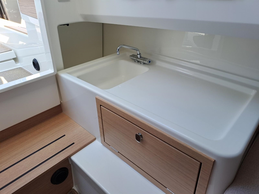 Modern boat interior featuring a sleek white sink, wooden cabinetry, and natural light from a nearby window.